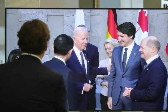 2022年3月24日，在比利時布魯塞爾的北約總部，一名男子觀看屏幕上美國總統(tǒng)拜登（右四）、歐盟委員會主席馮德萊恩（右三）、加拿大總理特魯多（右二）、德國總理朔爾茨（右一）出席七國集團(tuán)峰會合影儀式的畫面。新華社記者鄭煥松攝