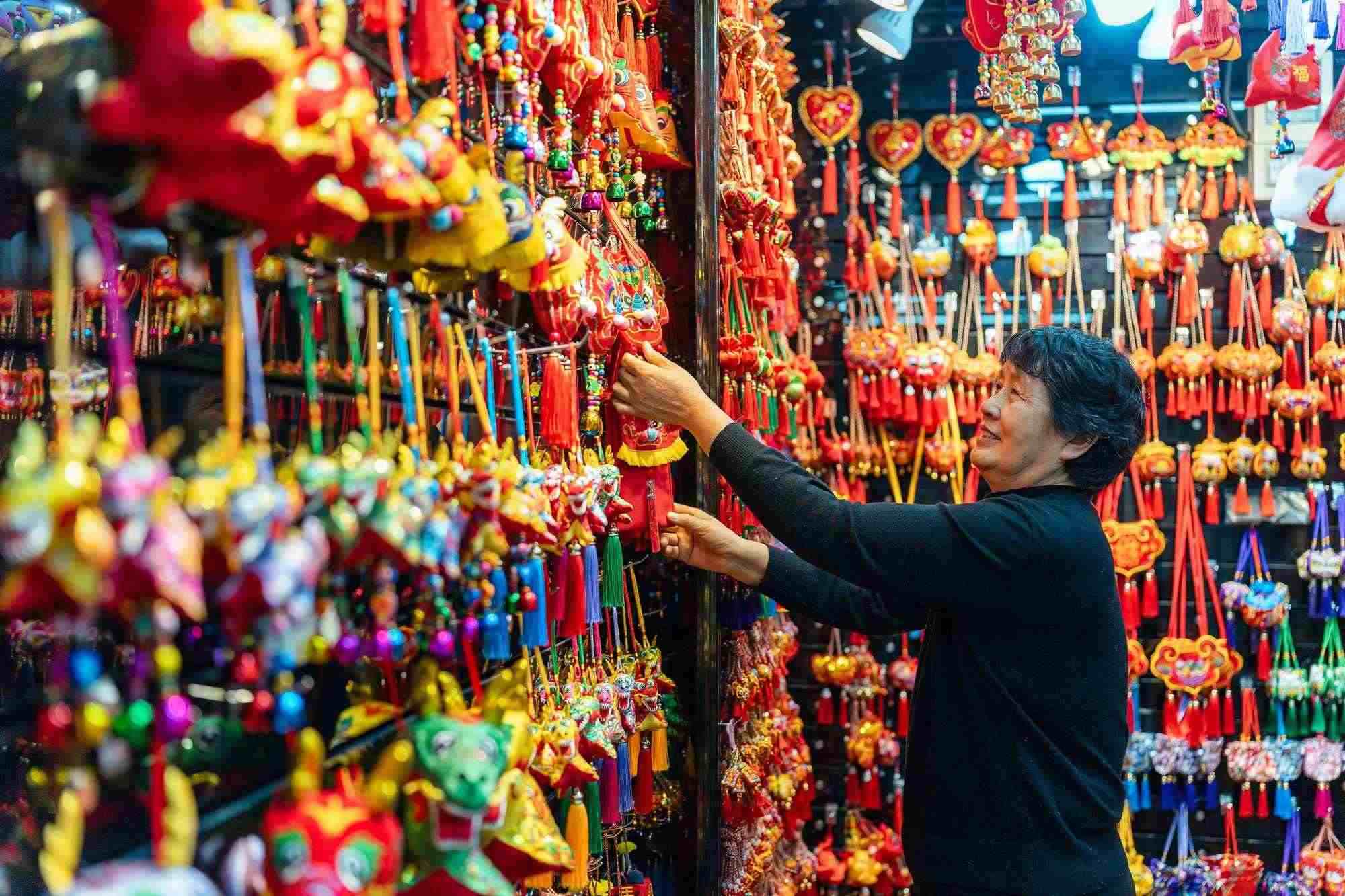 2023年12月11日，金華義烏國際商貿(mào)城，龍年喜慶用品掛滿攤位，顧客正在挑選中。