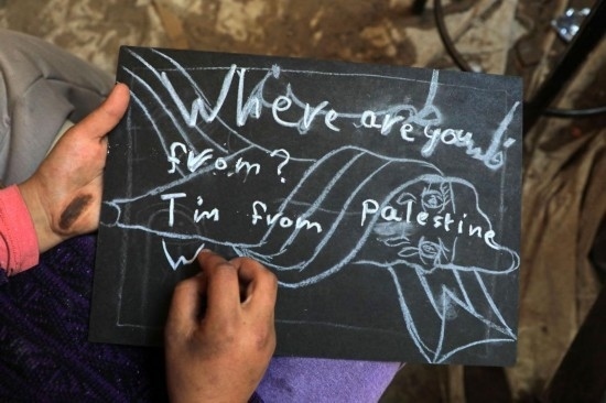 2023年12月28日，一名學(xué)生在加沙地帶南部城市拉法一所學(xué)校的臨時教室中寫下“我來自巴勒斯坦”的字樣。新華社發(fā)（里澤克·阿卜杜勒賈瓦德攝）