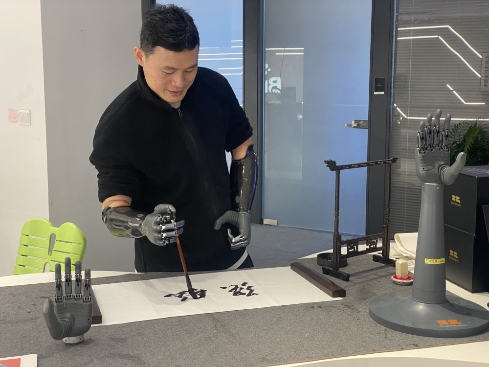 2024年3月29日，在浙江強腦科技有限公司展廳內(nèi)，失去雙手的產(chǎn)品體驗官倪敏成依靠智能仿生手寫毛筆字。新華社記者 魏一駿 攝
