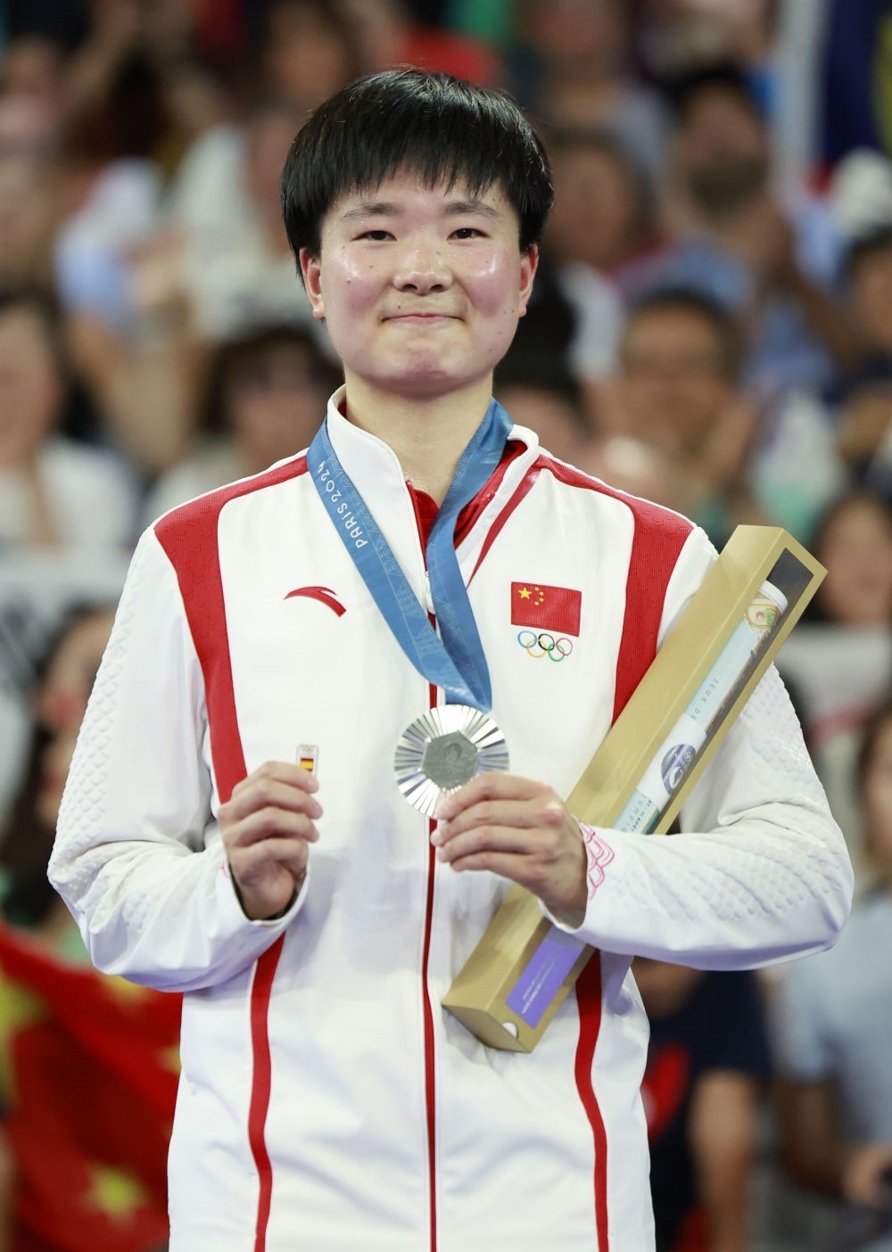 巴黎奧運(yùn)會(huì)羽毛球女子單打亞軍、中國選手何冰嬌在頒獎(jiǎng)儀式上一手握著銀牌，一手握著西班牙奧委會(huì)徽章（2024年8月5日攝）。新華社記者 任正來 攝