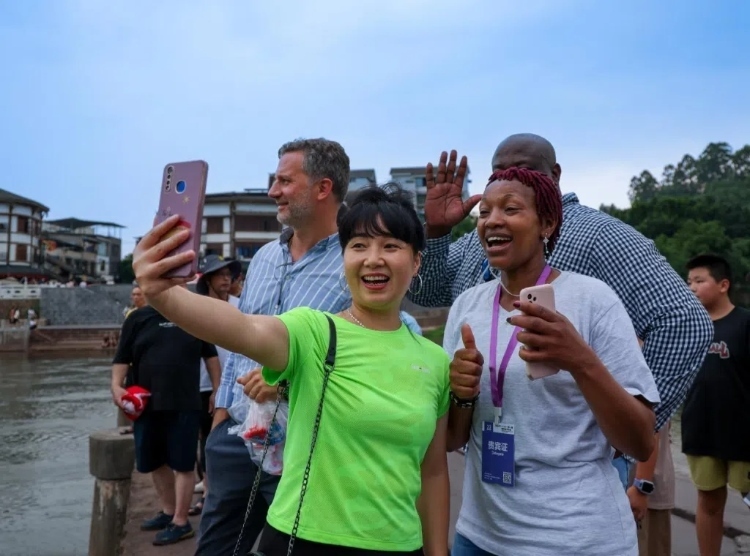 2024“一帶一路”媒體合作論壇聯(lián)合采訪調(diào)研行成員在樂山蘇稽古鎮(zhèn)與游客合影留念。本報記者 伊霄攝