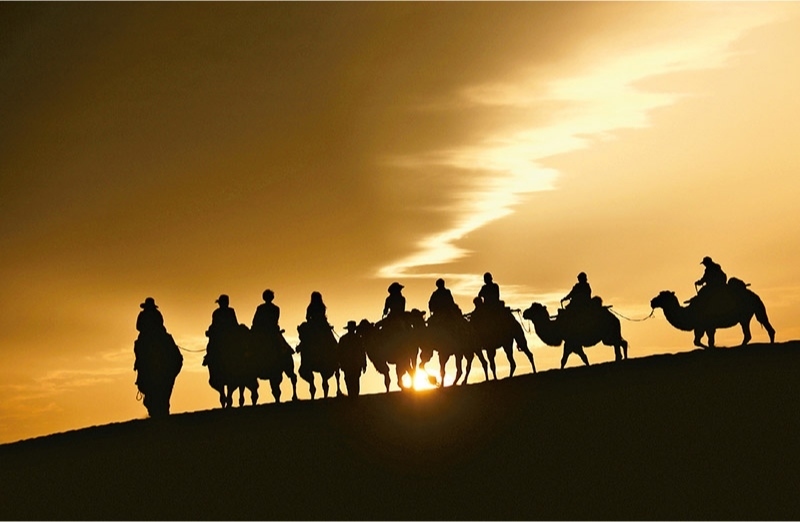 新時(shí)代以來(lái)，文化和旅游深度融合發(fā)展體制機(jī)制不斷健全，成功走出了一條獨(dú)具特色的中國(guó)旅游發(fā)展之路。圖為2024年9月1日清晨，游客在甘肅省敦煌市鳴沙山月牙泉景區(qū)乘騎駱駝，欣賞大漠風(fēng)光，體驗(yàn)絲路風(fēng)情。 新華社發(fā) 張曉亮/攝