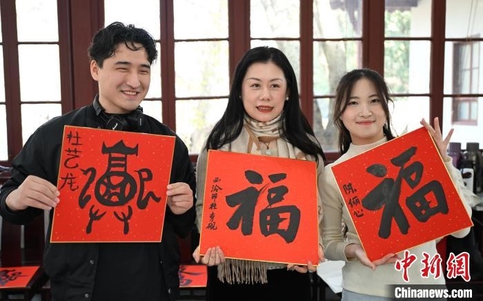 1月20日，外籍留學(xué)生和西泠印社社員李硯(中)展示各自創(chuàng)作的福貼。當(dāng)日，來(lái)自巴西、馬來(lái)西亞、加納、哈薩克斯坦的外籍留學(xué)生在浙江杭州西泠印社體驗(yàn)福貼、春聯(lián)和篆刻，感受古老的中國(guó)傳統(tǒng)文化。中新社記者 王剛 攝
